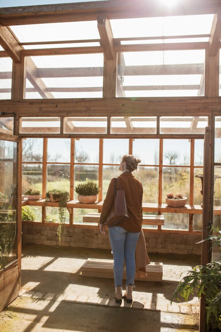 A Person Walking Through A Wooden Structure Filled With Plants At Cornerstone Gardens