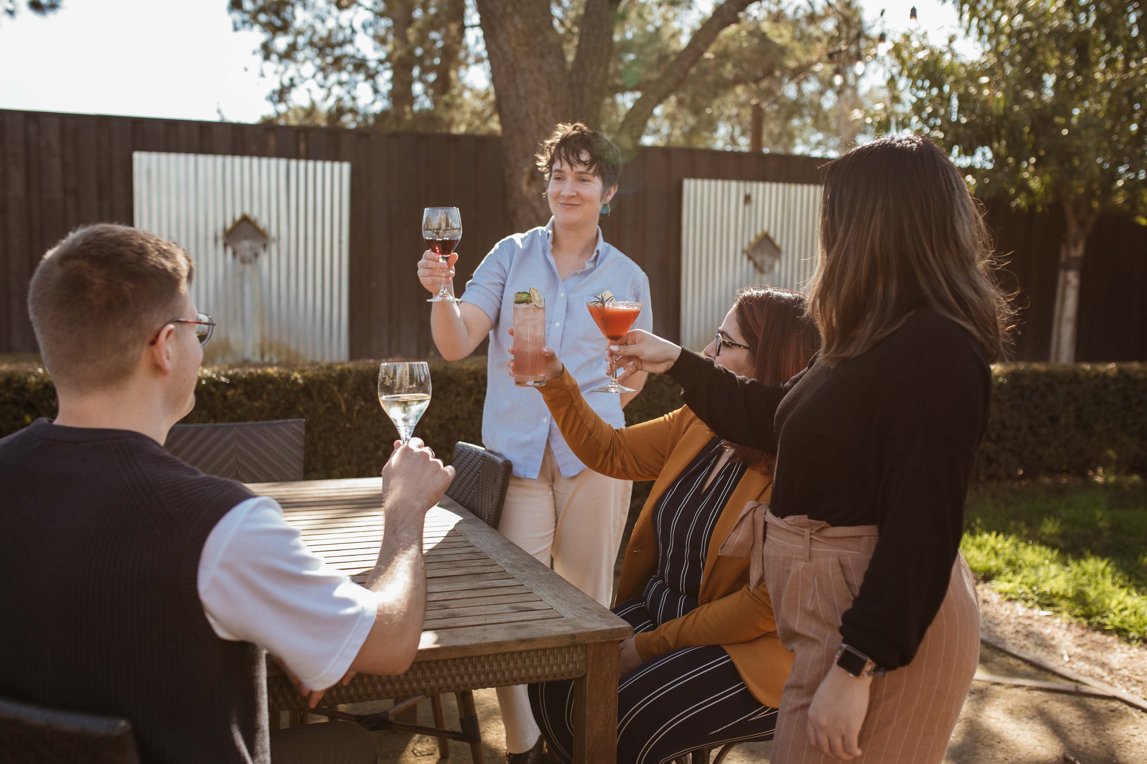 Four People Cheersing Their Drinks At An Outdoor Table